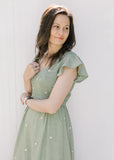Close up of smocked bodice, v-neck and flutter cap sleeves on a sage midi with cream flowers.